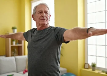 Homme âgé souriant faisant des exercices de maintien de l'équilibre dans un salon lumineux