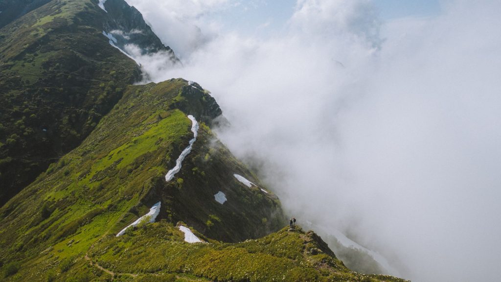 Deux randonneurs progressant sur une crête de montagne dans les nuages