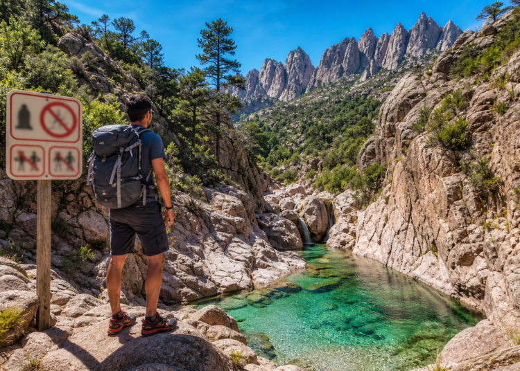 Randonneur devant un panneau de réglementation près d’un canyon turquoise en Corse, secteur Bavella Purcaraccia