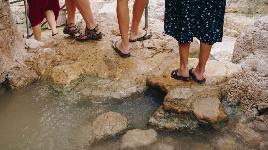 Randonneurs en sandales sur un passage rocheux au bord de l’eau