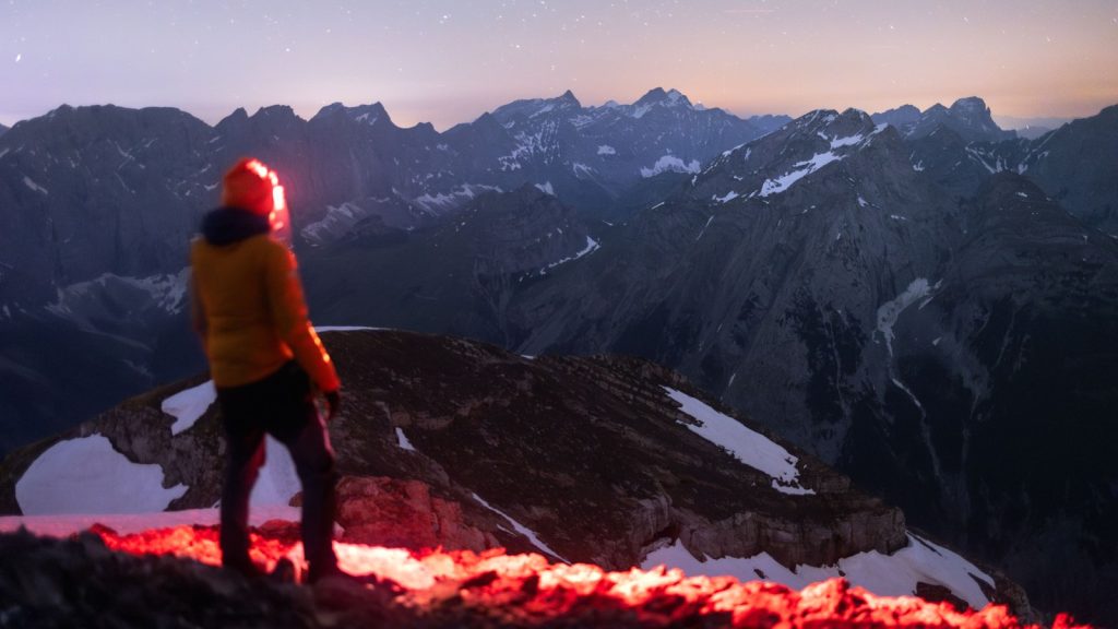 Randonneur avec lampe frontale face aux montagnes sous un ciel étoilé