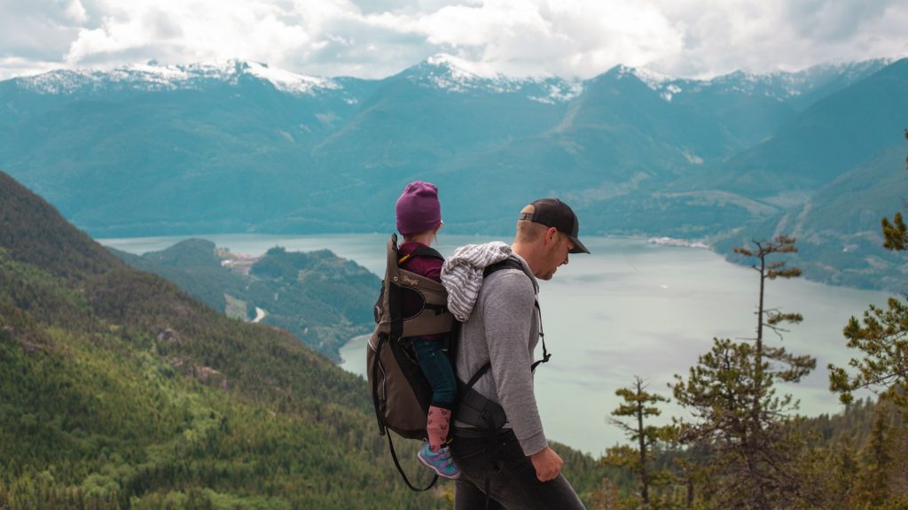 Parent portant un enfant dans un porte-bébé sur un sentier de montagne
