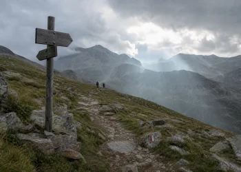 Sentier de montagne avec panneau directionnel sous un ciel changeant