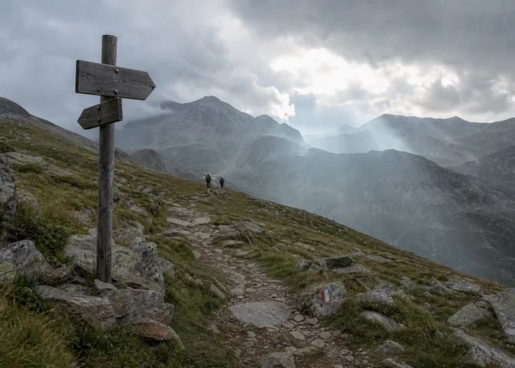 Sentier de montagne avec panneau directionnel sous un ciel changeant