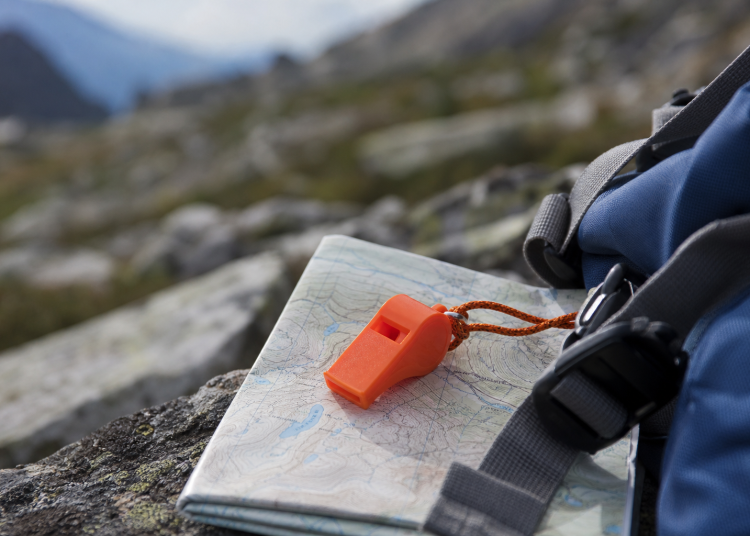 Sifflet orange de sécurité posé sur une carte de randonnée en montagne