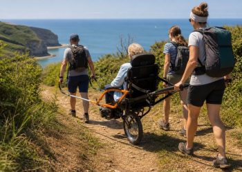 Personne âgée accompagnée sur un sentier côtier dans un fauteuil tout-terrain à roue centrale