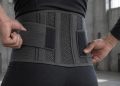 Mains ajustant une large ceinture de maintien lombaire sur un bas du dos, atelier en arrière-plan