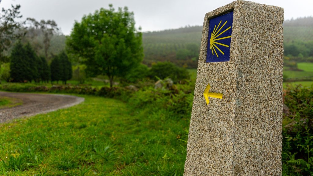 Borne de pierre du chemin de Compostelle avec le coquillage jaune et la flèche directionnelle
