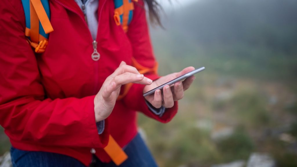 Randonneur en veste rouge consultant une carte sur son téléphone en montagne