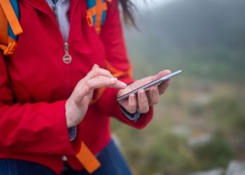 Randonneur en veste rouge consultant une carte sur son téléphone en montagne