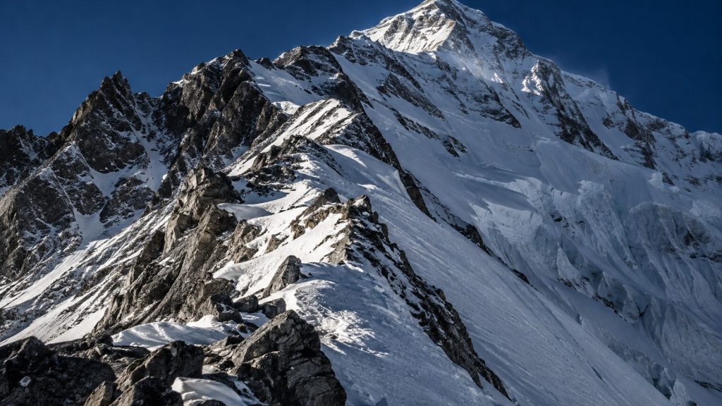 Crête rocheuse enneigée de haute altitude sous un ciel profond, pente raide et séracs, ambiance minérale extrême