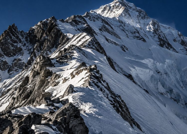 Crête rocheuse enneigée de haute altitude sous un ciel profond, pente raide et séracs, ambiance minérale extrême