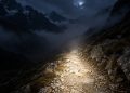 Faisceau de lampe frontale éclairant un sentier rocheux de montagne dans la nuit, brume et pentes sombres de part et d'autre